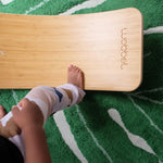 Close up of a childs foot on a Wobbel Bamboo balance board on a green leaf carpet