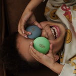 A child happily holding two of the Wobbel Candy Drops up to their eyes. The Candy Drops in the photo are from the Bombai set. Perfect for balancing