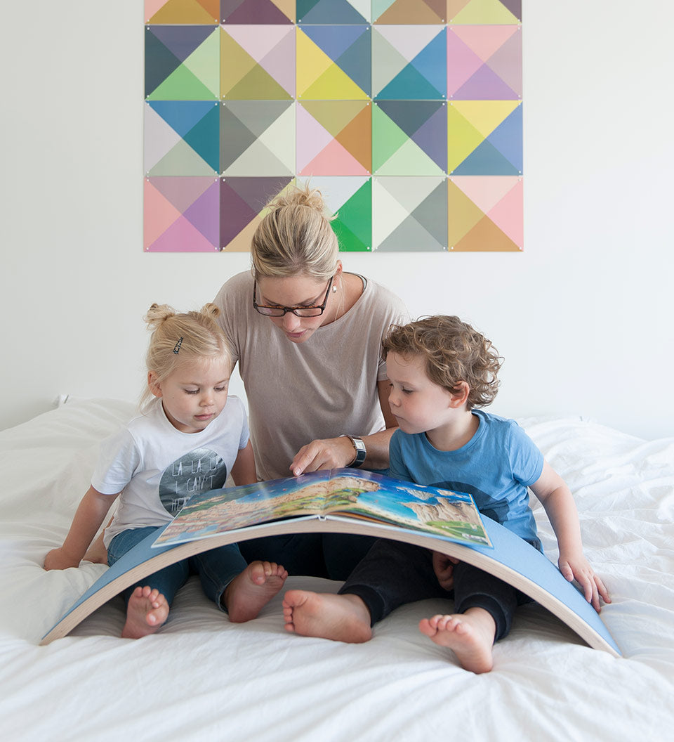 Woman and two children reading a book on a Wobbel XL felted balance board on a bed