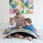 Woman and two children reading a book on a Wobbel XL felted balance board on a bed