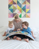 Woman and two children reading a book on a Wobbel XL felted balance board on a bed