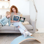 Lady reading child a book using the Wobbel XL Beech Wood balance board as a foot rest in a living room