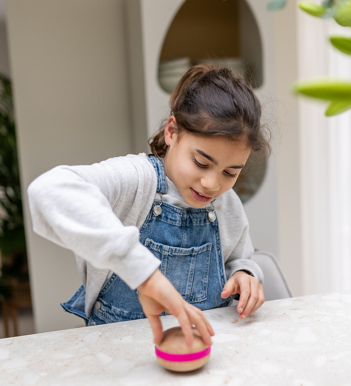 A child playing and spinning a Wooden Wobbel Candy Big Macaron on a  table. Made from Beech wood with a pink "filling"