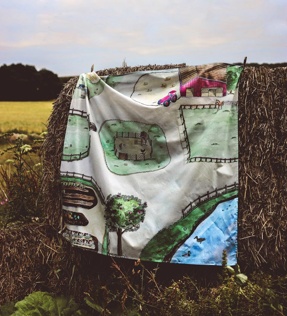 Wondercloths childrens eco-friendly farm print play cloth hanging over a bail of hay in a field