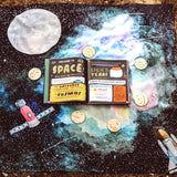 Wondercloths childrens large space print play silk laid out on a woodland floor with a space book on top