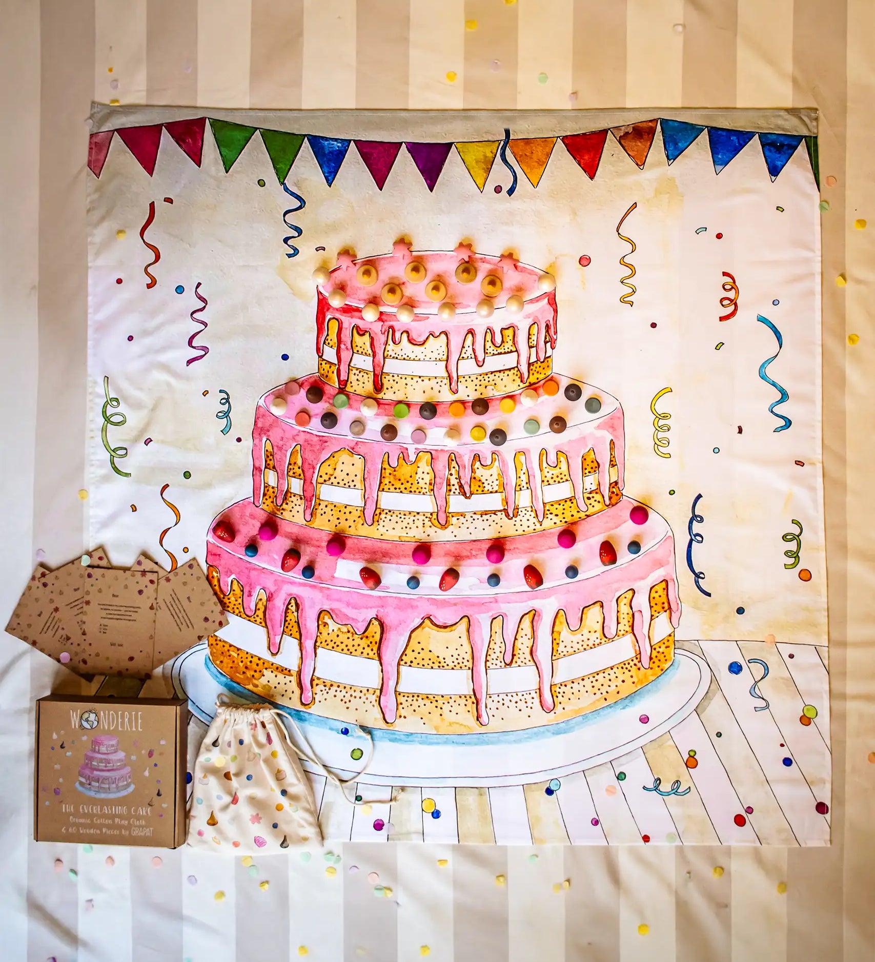 Wonderie play cloth the everlasting cake play set containing a square cloth with an iced three tier cake illustration and a set of Grapat loose parts to decorate it with. 
