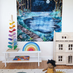 The Wonderie moonlight forest design play cloth hung up on the wall in a playroom. The PlanToys Victorian dolls house, Magic Wood marble tree and the Gwawr rainbow are placed in front. An Olli Ella doll can be seen sitting on the floor at the front on a rug. 