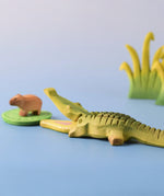 Bumbu Toys' Wooden Crocodile with it's mouth open, in a scene with Bumbu's Capybara, Reeds in large and small, and a Lilypad.