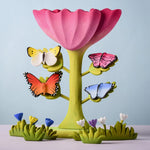 Bumbu Toys wooden Butterflies placed on a Bumbu Pink Flower, surrounded by Bumbu flowers and grass.
