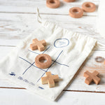 The Cotton drawstring storage bag placed on a white wooden surface with pieces from the Wooden Story Tic Tac Toe game placed on the printed grid on the bag. 
