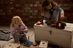 2 children playing with the Wooden Story 30 Rainbow Blocks in Tray. One child is sat on the floor the other is sat on top of a painted wooden chest. 