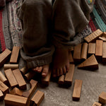 A close up of a child's feet resting on Wooden Story building blocks. 