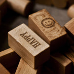 A close up of the blocks from the Wooden Story 72 XL Peace & Love Blocks set. There are two block on the top with etched details, one has a simple smiley face the other has the word happy written on it in capital letters. 
