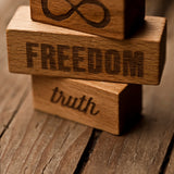 A close up of three blocks from the Wooden Story 72 XL Peace & Love Blocks set. One block has the infinity symbol, one has the word freedom and the third has the word truth etched on. 