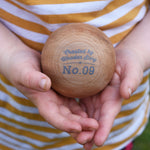 A close of of a wooden boules ball in a child's hand. The words 'created by Wooden Story and No.9 can be seen printed in grey on the ball. 