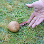 A close up of an adult's hand throwing one of the boules balls on grass. 