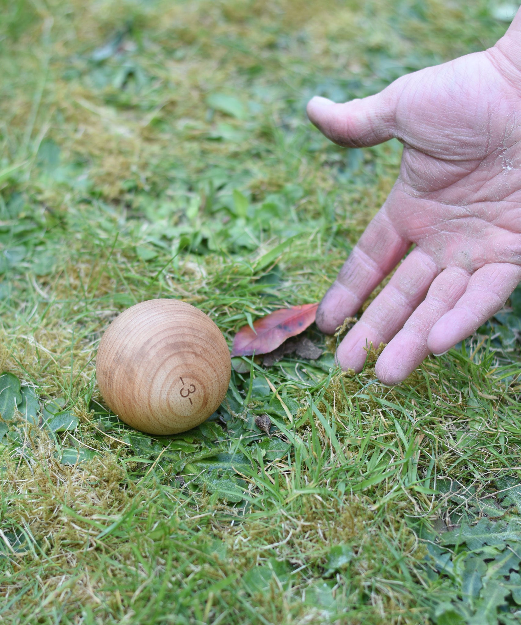 A close up of an adult's hand throwing one of the boules balls on grass. 