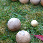 Two boules balls from the Wooden Story boules set on grass next to the small jack ball. Other boules balls can be seen in the background. 