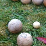 Two boules balls from the Wooden Story boules set on grass next to the small jack ball. Other boules balls can be seen in the background. 
