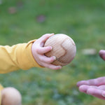 A close up of a Wooden Story boules ball in a young child'd hand. They are passing the ball over.