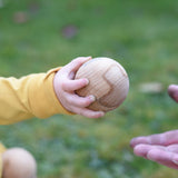 A close up of a Wooden Story boules ball in a young child'd hand. They are passing the ball over.