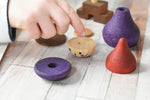 A close up of a child's hands placing the pieces from the Wooden Story Stacking Toy Stick Purple Number 6 Figure on a wooden surface.