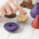 A close up of a child's hands placing the pieces from the Wooden Story Stacking Toy Stick Purple Number 6 Figure on a wooden surface.