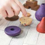 A close up of a child's hands placing the pieces from the Wooden Story Stacking Toy Stick Purple Number 6 Figure on a wooden surface.