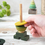 A close up of a child playing with the Wooden Story green stick figure stacking toy, the child is placing a piece on the stack.