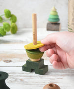 A close up of a child playing with the Wooden Story green stick figure stacking toy, the child is placing a piece on the stack.