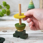 A close up of a child playing with the Wooden Story green stick figure stacking toy, the child is placing a piece on the stack.