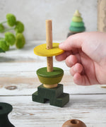 A close up of a child playing with the Wooden Story green stick figure stacking toy, the child is placing a piece on the stack.