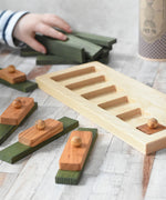 The Wooden Story Long Short Puzzle placed on a wooden surface. The base frame has one piece in it the other have been placed on top of green coloured Kapla blocks.