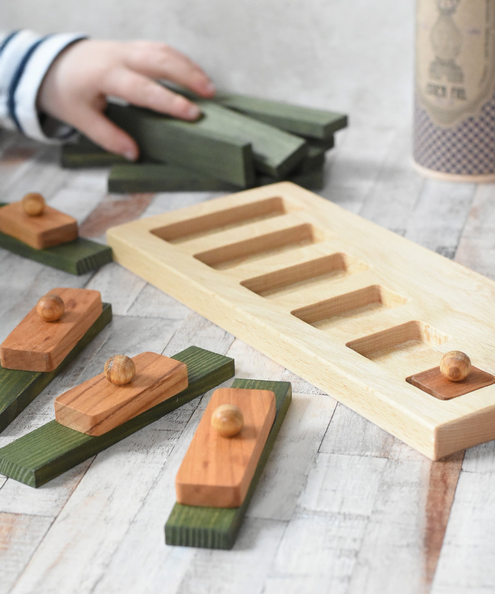 The Wooden Story Long Short Puzzle placed on a wooden surface. The base frame has one piece in it the other have been placed on top of green coloured Kapla blocks.