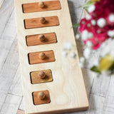 The Wooden Story long short traditional style puzzle toy placed on a wooden surface, flowers can be seen in the foreground. 