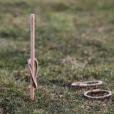 The Wooden Story Loop Toss game set up on grass outdoors. One loop can be seen on the stick with two others laying on the grass besides the stick.