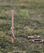The Wooden Story Loop Toss game set up on grass outdoors. One loop can be seen on the stick with two others laying on the grass besides the stick.