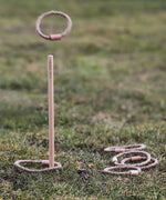 The Wooden Story Loop Toss game set up on grass outdoors. A rope loop  can be seen mid air.