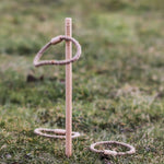 The Wooden Story Loop Toss game set up on grass outdoors. One loop can be seen mid air with two other laying on the grass besides the stick.