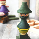 The Wooden Story green stick figure stacking toy on a wooden surface. It's box can be seen in the background along with the purple coloured stick figure. 