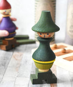 The Wooden Story green stick figure stacking toy on a wooden surface. It's box can be seen in the background along with the purple coloured stick figure. 