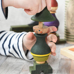 A close up of a child playing with the Wooden Story green stick figure stacking toy, the child is lifting the top, hat shaped piece off the stack.