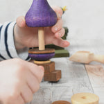 A close up of a child's hand playing with the Wooden Story Stacking Toy Stick Purple Number 6 Figure. They are lifting a purple coloured piece off the base pole.