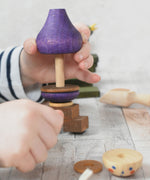 A close up of a child's hand playing with the Wooden Story Stacking Toy Stick Purple Number 6 Figure. They are lifting a purple coloured piece off the base pole.