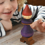 The Wooden Story Stacking Toy Stick Purple Number 6 Figure on a wooden surface. A smiling child can be seen in the background. 