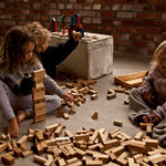 Children sitting on a floor playing with blocks from various Wooden Story block set. The three children are surrounded by blocks of different sizes and shapes. 