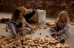 Children sitting on a floor playing with blocks from various Wooden Story block set. The three children are surrounded by blocks of different sizes and shapes. 