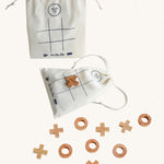 Wooden Story Tic Tac Toe game on a plain background. The wooden X and O pieces are spread out besides the drawstring bag which has the grid printed on it. One wooden X cross piece has been placed on the grid in the centre of the bag. 