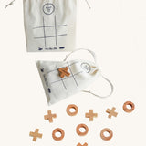Wooden Story Tic Tac Toe game on a plain background. The wooden X and O pieces are spread out besides the drawstring bag which has the grid printed on it. One wooden X cross piece has been placed on the grid in the centre of the bag. 