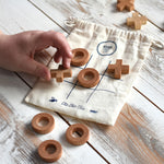 A close up of a child's hand playing with the Wooden Story Tic Tac Toe game.